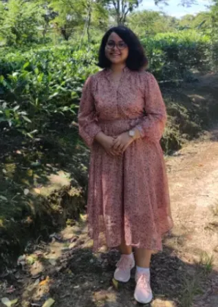Student standing in forested area smiling at camera.