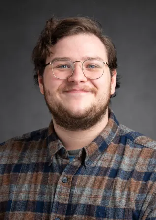 A man with short wavy hair, wearing a buttoned up flannel shirt and a pair of glasses.
