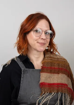A women wearing overalls and a scarf draped over her shoulder smiling politely 