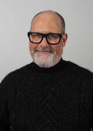 David Swenson wearing thick brimmed black glasses and a black sweater.