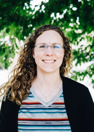 A woman stands smiling in front of a tree
