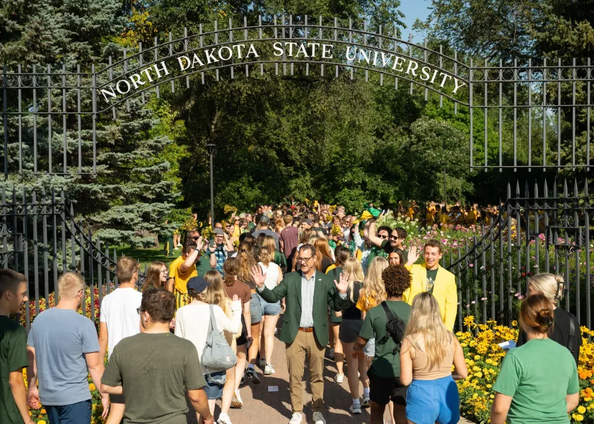 A photo of NDSU students walking through the main gate, high-fiving President David Cook