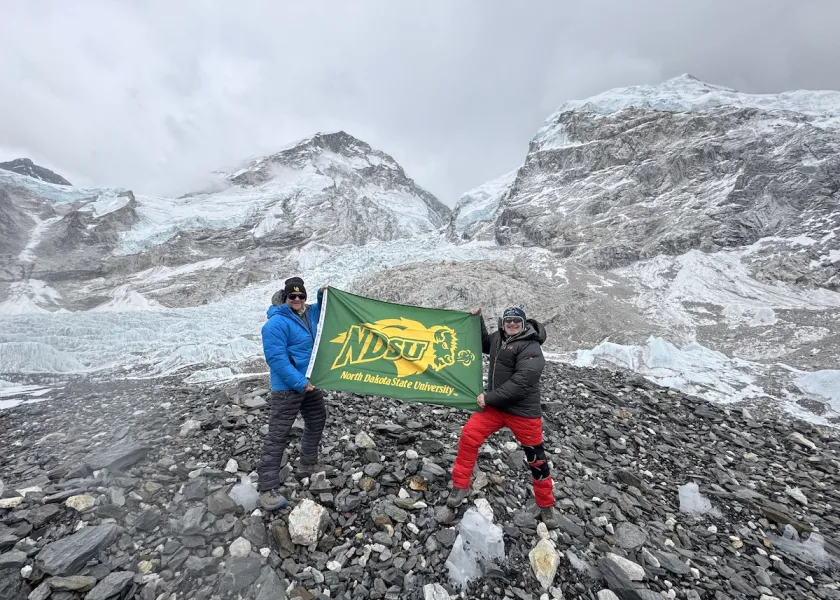 NDSU alum, Lee Hoedl pictured in red climbing pants, holds the NDSU flag at the base of the Khumbu Icefall.