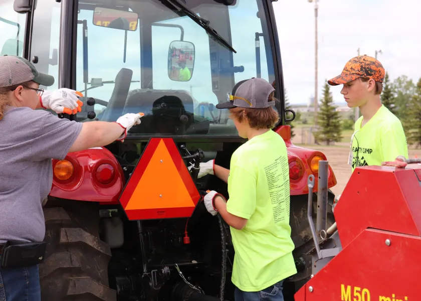 Teen farm safety camp participants demonstrate how to properly connect hydraulic hoses and power take-off shafts of farm equipment to a tractor.