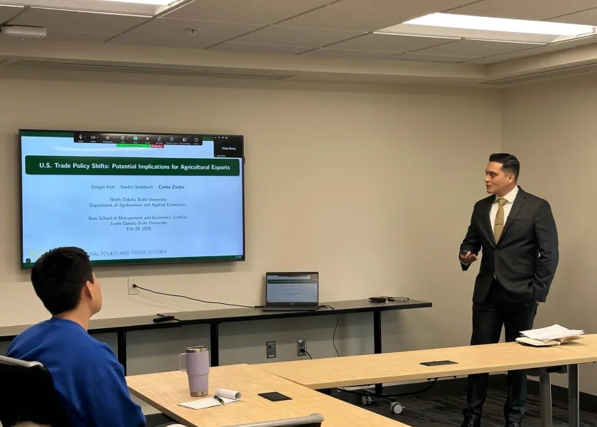 Carlos Zurita, senior research economist with NDSU’s Center for Agricultural Policy and Trade Studies, stands at the front of a room giving a presentation.