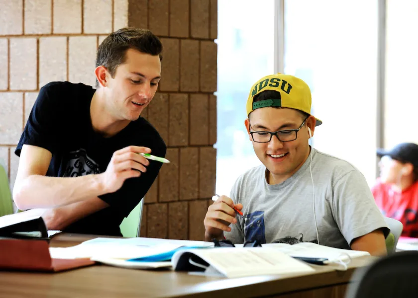 two students doing work together at a table in the library