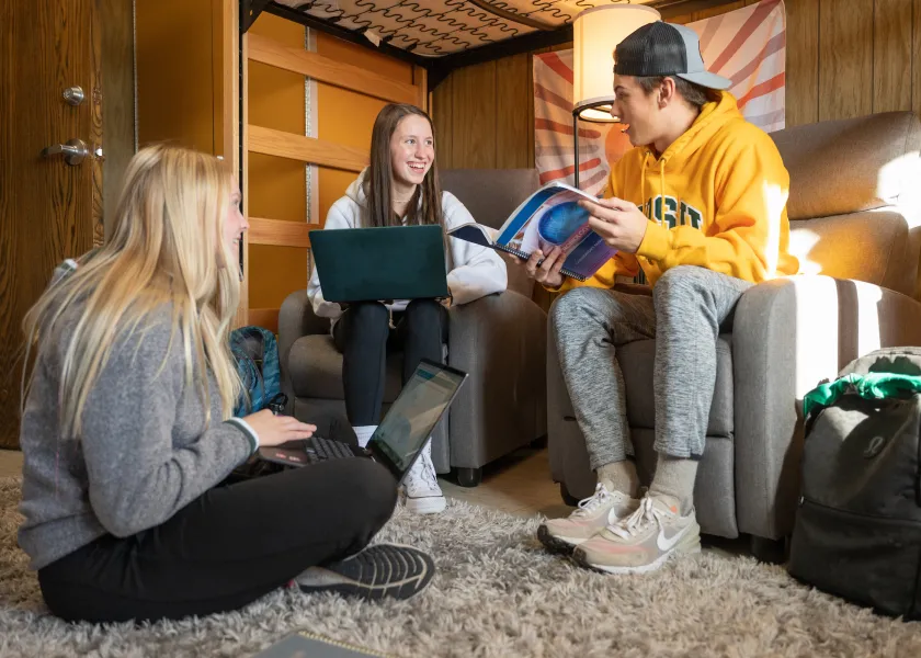 2 female students and one male student talking while sitting in chairs and on floor
