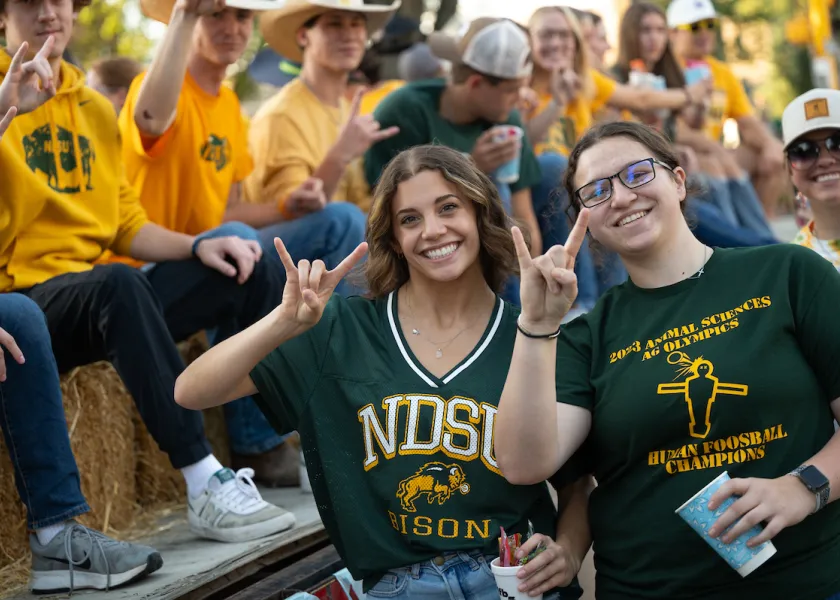 Students holding bison horns up in front of float at homecoming parade