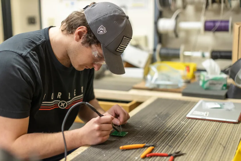 student working on a circuit board with a soldering iron