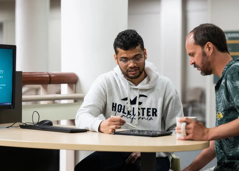 student working with a professor reviewing a project on a tablet