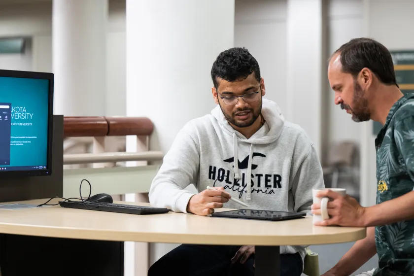 student working with a professor reviewing a project on a tablet