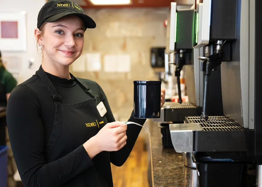 Dining worker at the Bison Beanery making a coffee holding a ticket