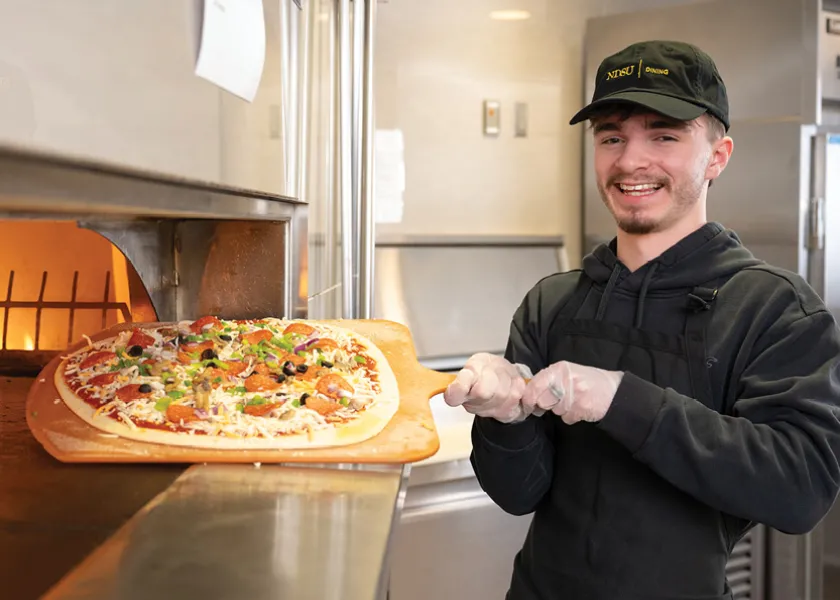 Dining worker holding a pizza about to go in the oven