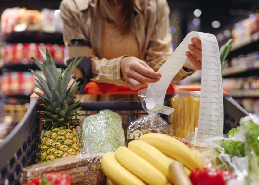 A woman holds a receipt while pushing a cart full of groceries.