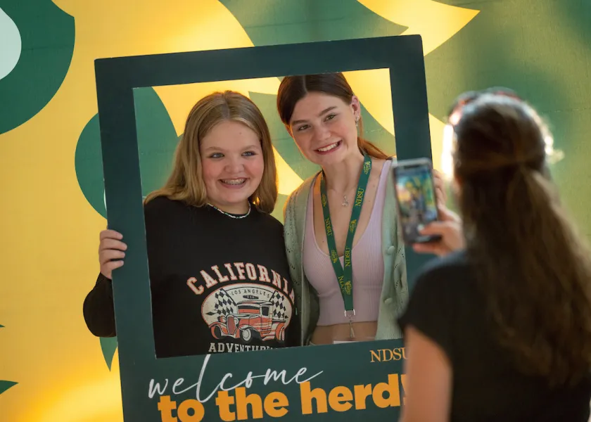 students holding a polaroid cutout frame that says Welcome to the Herd