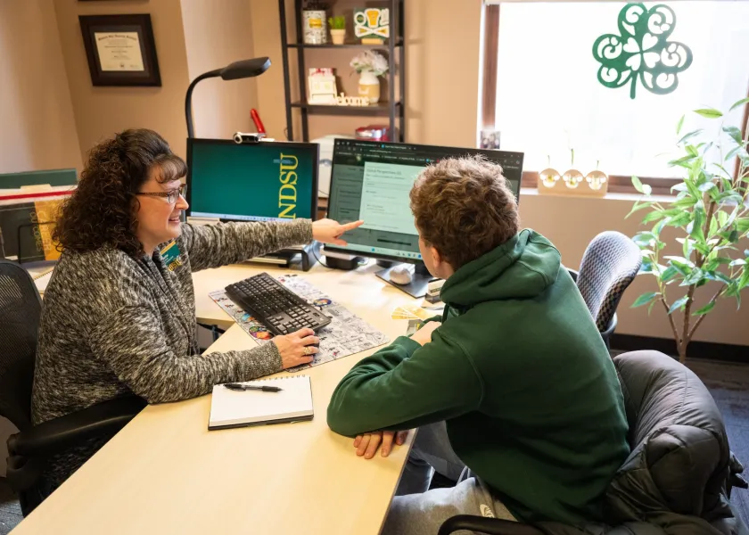 Patti Seidler, an NDSU professional advisor, sits at her desk with a student.