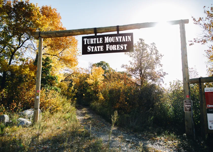 A sign that reads "Turtle Mountain State Forest" hung in front of a nature trail