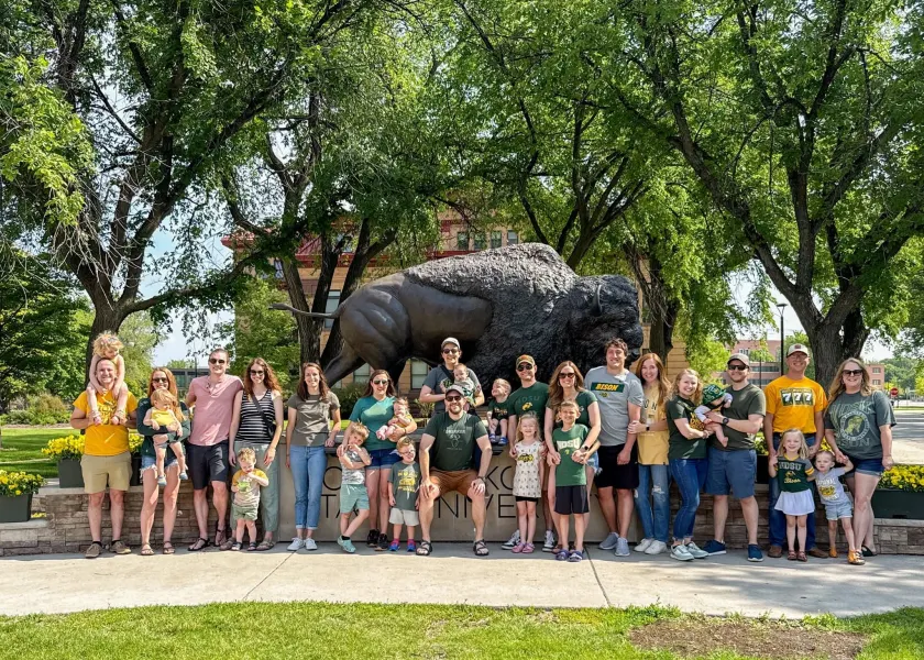 A group of NDSU alum and friends stand in front of the Bison statue on NDSU's campus.