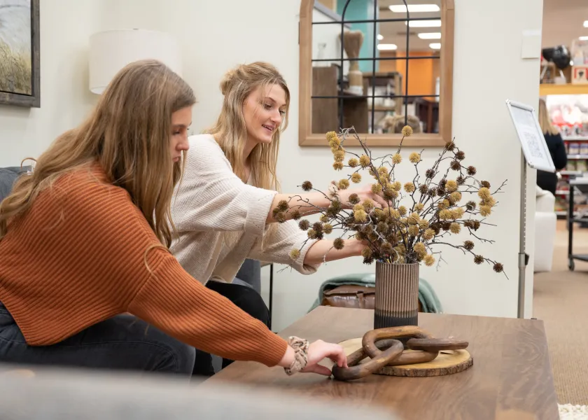 Two interior design students decorate a table with a vase and flowers.
