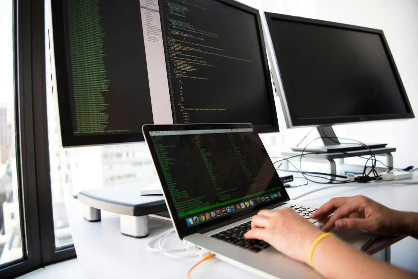 close up of hands on a laptop keyboard with multiple computer monitors in the background