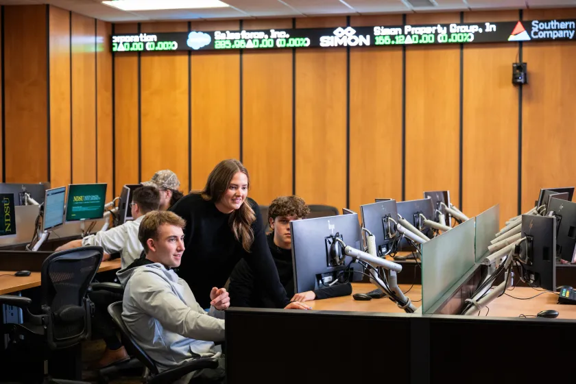 business students gathered around a computer in the trading room