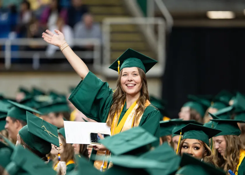 A graduating NDSU student waves at the crowd during the spring commencement ceremony in the Fargodome.