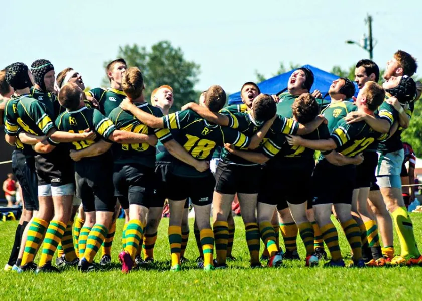 rugby players in green and yellow uniforms cheering in a circle