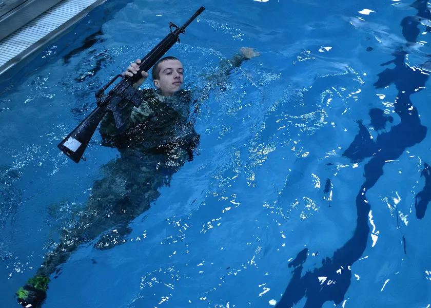 Army ROTC Cadet participating in the Combat Water Survival Test in full uniform and weapon.