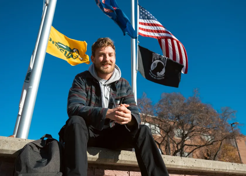 Samuel Sveen, U.S. Air Force veteran and NDSU student, poses for a photo by a flag post on campus.