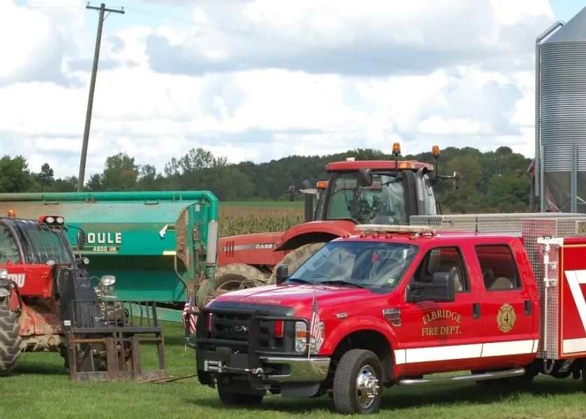 A fire engine parked next to some farm equipment with a grain silo in the background