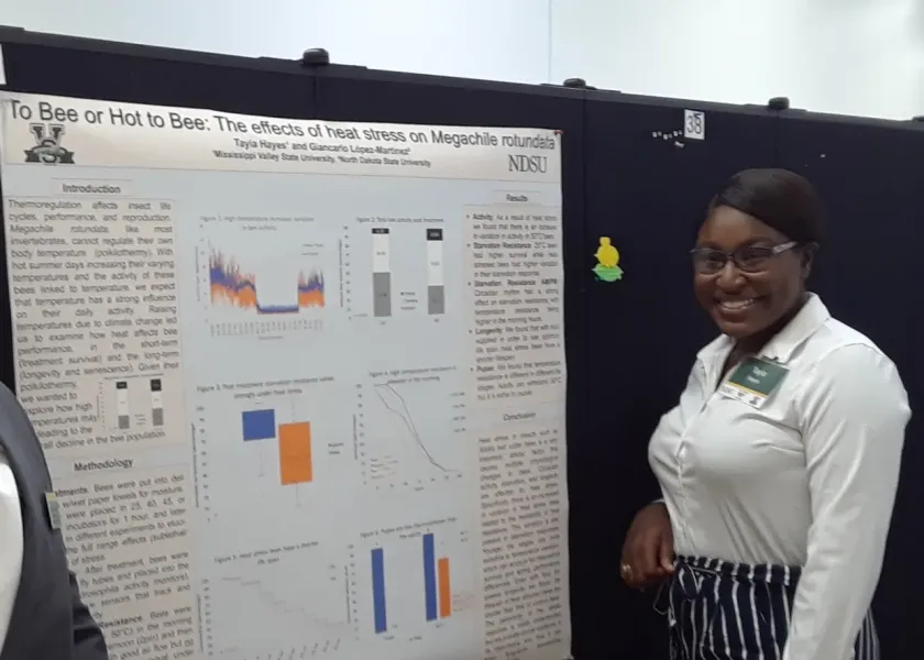 Tayia standing next to her research poster smiling at camera.