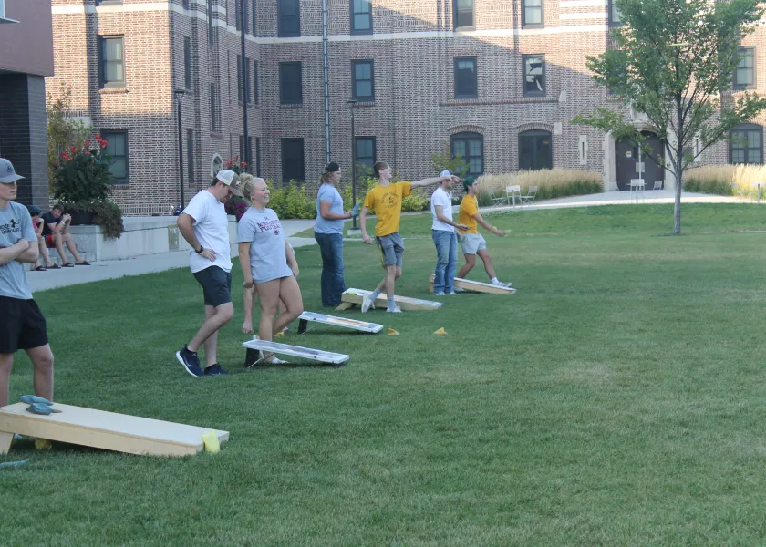 NDSU Students standing outside on Churchill Field dressed in spring clothing playing bean bag toss