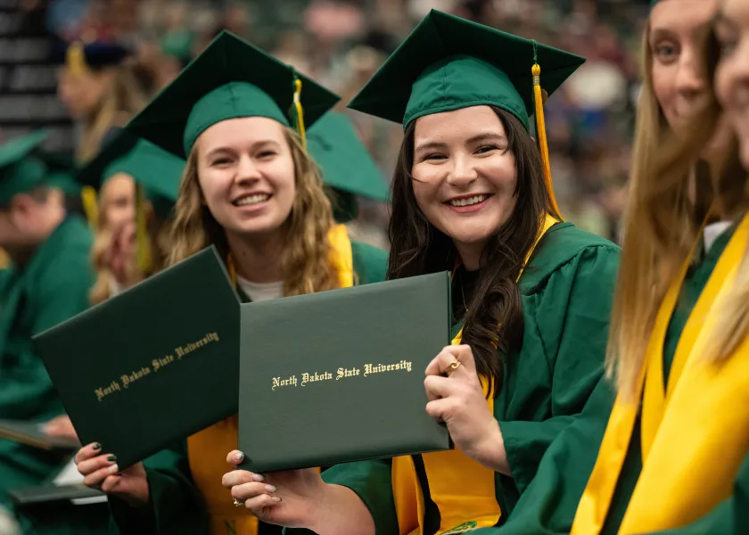 Two NDSU students pose for a photo at the fall commencement ceremony while wearing their caps and gowns.
