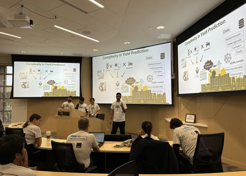 Students present on yield prediction in a classroom while attendees watch slides on large screens.