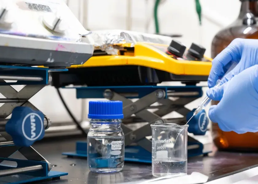 a researcher wearing gloves removes liquid from a flask using a hypodermic needle