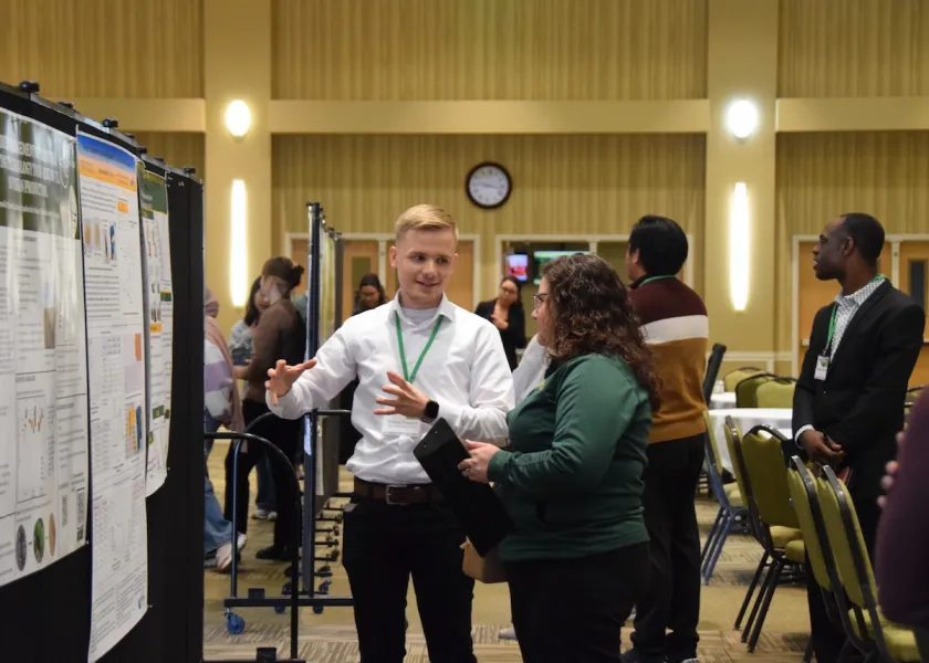 An NDSU student explains his research with a posterboard.