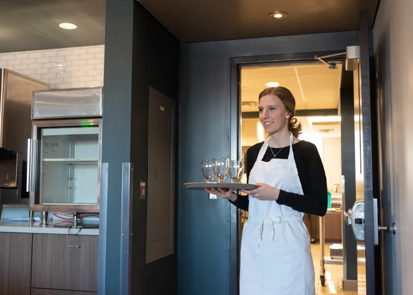 A student in the nutrition program carries a platter with glasses on it in the 800 café.