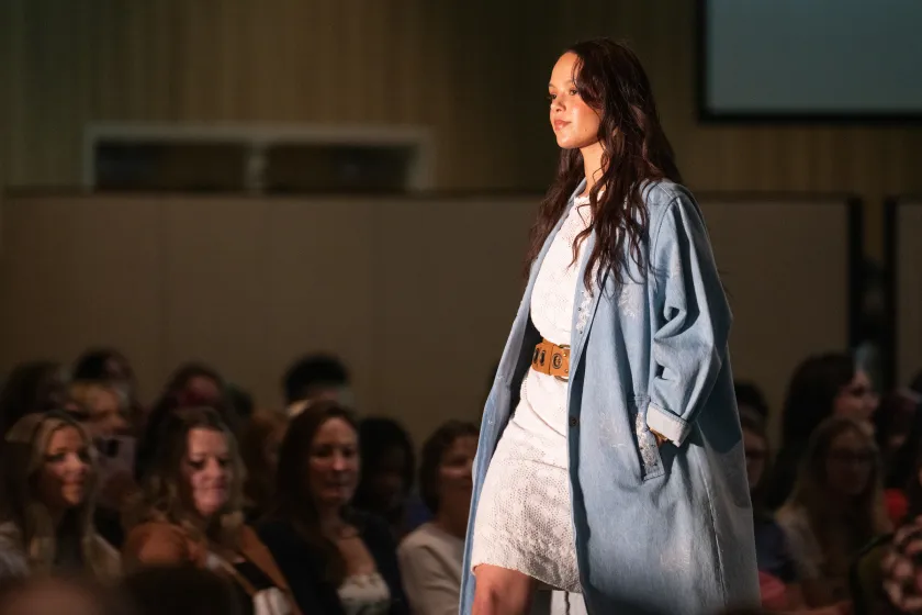 Model walking in a white dress with a duster jean jacket at the 2025 NDSU Fashion show.