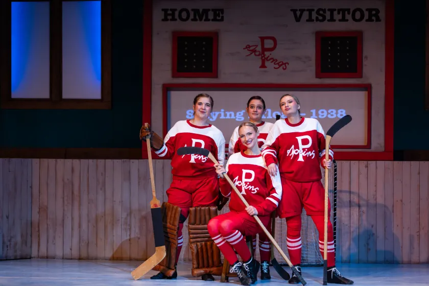 Four female students performing in Theatre NDSU's "Glory". The actors are wearing red and white hockey uniforms from the 1930s and holding hockey sticks.