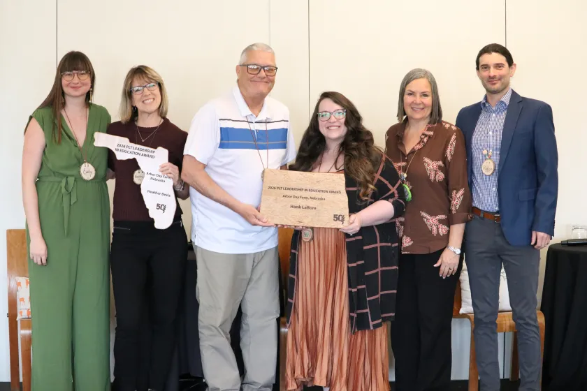 Hank LaBore holds a wood plaque alongside Beth Hill, North Dakota PLT Coordinator, and is surrounded by PLT National staff on the right and the other Leadership in Education Award winner on the left.