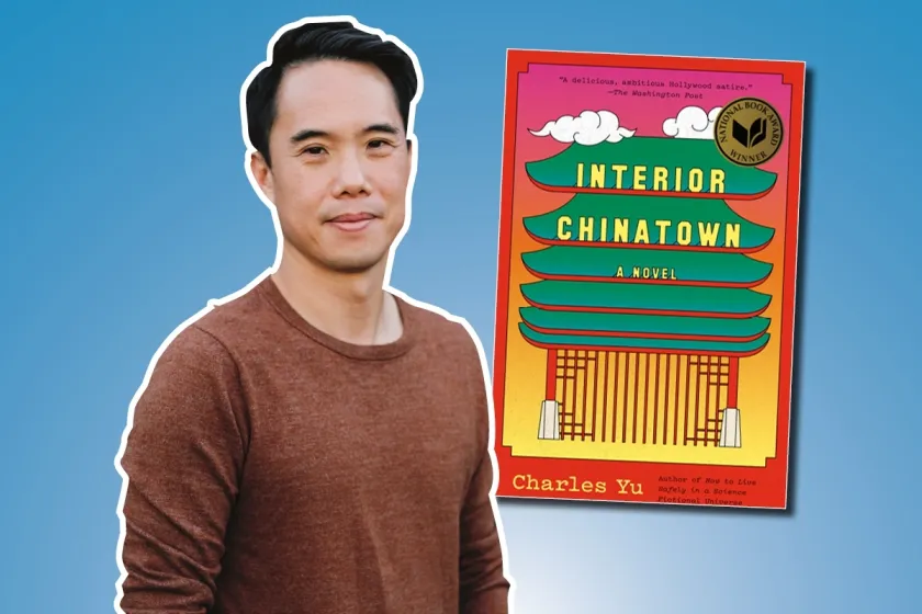 Charles Yu smiling at camera with book next to him