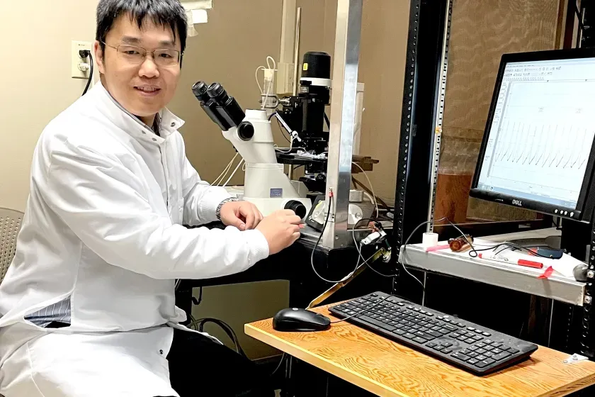 NDSU associate professor of pharmaceutical sciences, Ang Guo, sits at a desk in his lab.