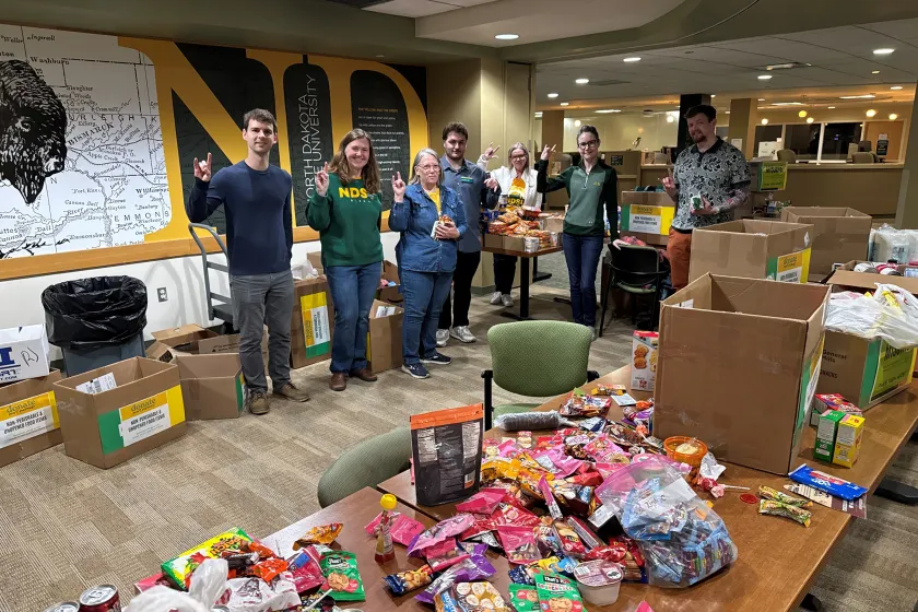 A group of people stand in from of tables full of food items. 