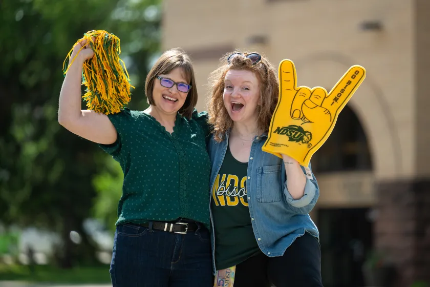 Angela Seewald-Marquardt and Maggie Latterell pose with Bison spirit items in front of Old Main