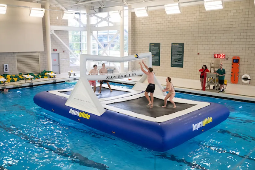 Students in swimsuits on a inflated, floating volleyball court in the middle of an indoor pool bumping the volleyball 