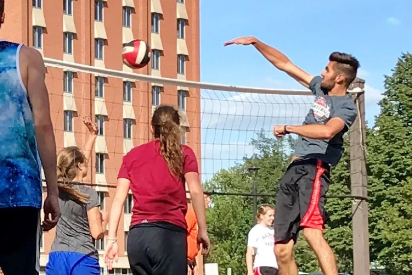 man jumping in front of volleyball next on sand court