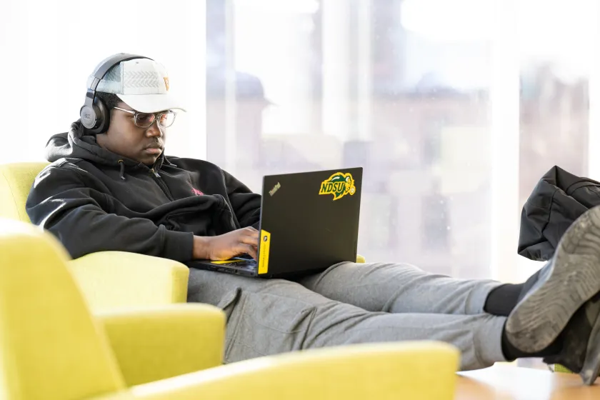 A student sits in a chair while typing on his laptop.