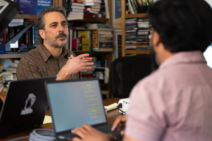 University Distinguished Professor of psychology, Michael D. Robinson, sits at a desk talking with students.