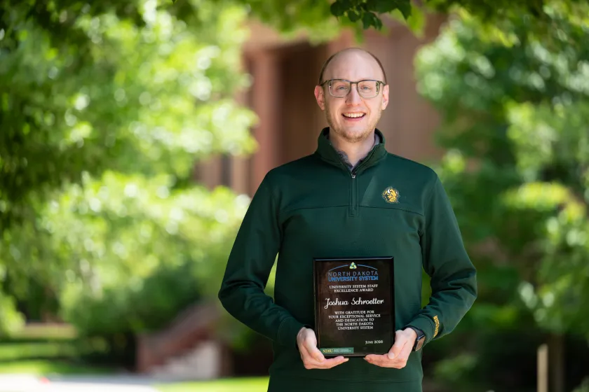 Shwa Schroetter holds up his NDUS Staff Excellence award plaque