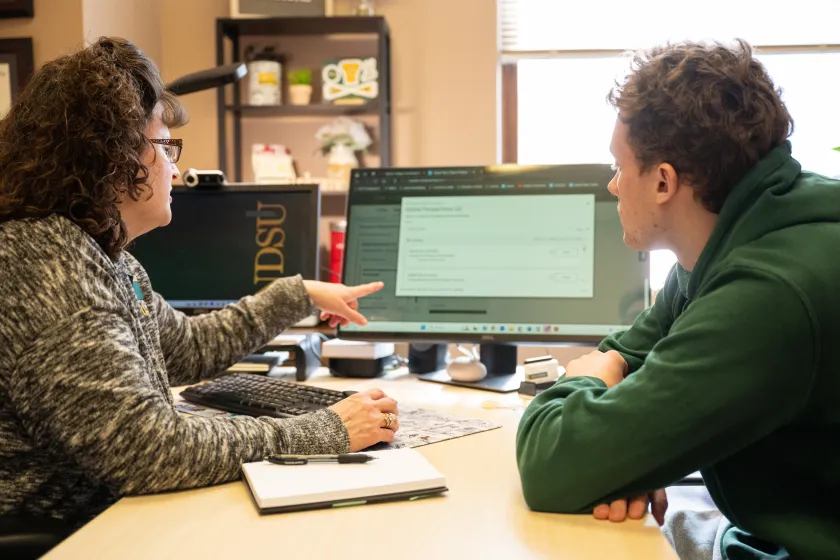 An NDSU staff member and student sit at a desk while looking at a computer